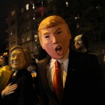 David Jiang, wearing a Donald Trump mask, and his girlfriend Kaja Klupinska, wearing a Hillary Clinton mask, left, make their way up Sixth Avenue during the Greenwich Village Halloween Parade, Saturday Oct. 31, 2015, in New York.  (AP Photo/Tina Fineberg)