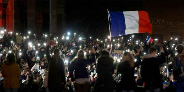 People, many of whom are French, hold up their lit phones as they take part in a vigil in solidarit...