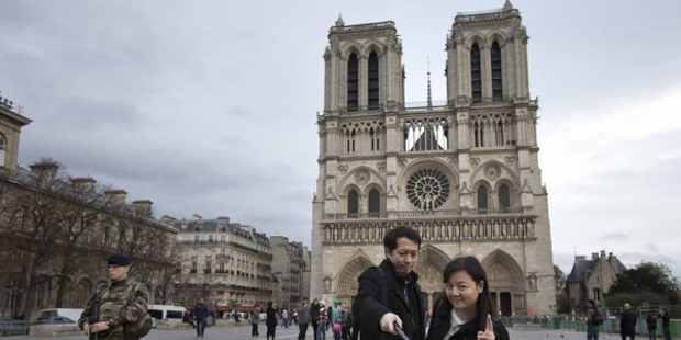 Tourists pose for a selfie while a French soldier patrols at Notre Dame cathedral in Paris, Monday,...