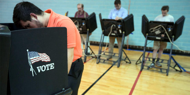 A voter, at left, fills out a paper ballot as electronic voting machines are used behind him at the...