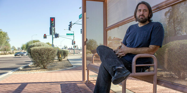 Drew Rodriguez sits at a bus stop outside the extended-stay hotel where he lives in north Phoenix o...