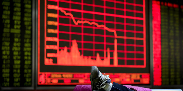 An investor places her leg on a bench near an electronic board displaying stock prices at a brokera...