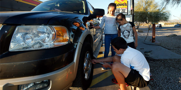 Ruben, 12, Niobe 7, and Ailani, 10, from California, help their mother put air in their car's tires...