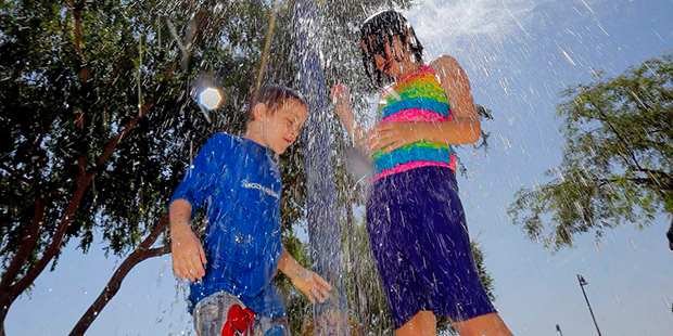 Alex Glaze and her brother Zane Glaze keep cool as they play under a water pipe, Tuesday, June 21, ...