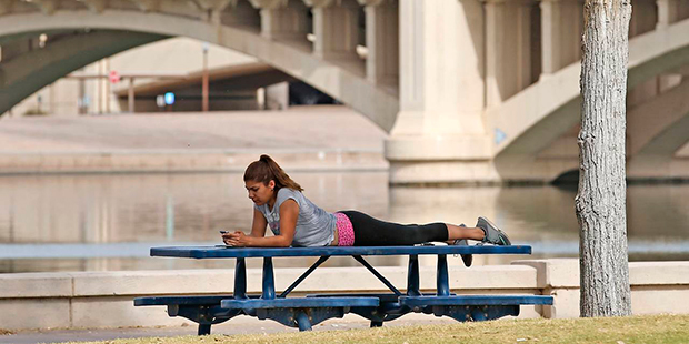 A woman relaxes next to Tempe Town Lake as temperatures are expected to break records again in Temp...