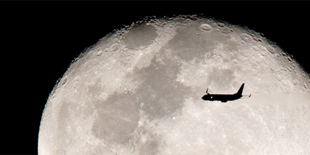 An airplane flies against the backdrop of the rising moon after taking off from Miami International...