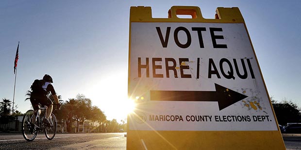 A cyclist rides past a sign directing voters to a primary election voting station early Tuesday, Au...