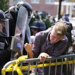 An white nationalist demonstrator is pushed out of the park by police at the entrance to Lee Park in Charlottesville, Va., Saturday, Aug. 12, 2017.  Gov. Terry McAuliffe declared a state of emergency and police dressed in riot gear ordered people to disperse after chaotic violent clashes between white nationalists and counter protestors. (AP Photo/Steve Helber)