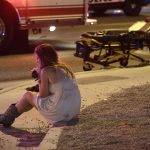 A woman sits on a curb at the scene of a shooting outside a music festival on the Las Vegas Strip on Oct. 2, 2017. (AP Photo/John Locher)
