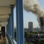 A resident in a nearby building watches smoke rise from the Grenfell Tower on fire in London on June 14, 2017. A massive fire raced through the high-rise apartment building in west London, killing at least 80 people and injuring many others. (AP Photo/Matt Dunham)
