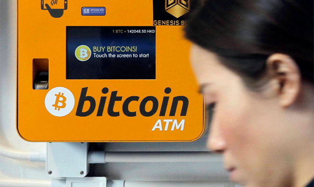 FILE - In this Dec. 21, 2017 file photo, a woman walks past the Bitcoin ATM in Hong Kong. The growt...