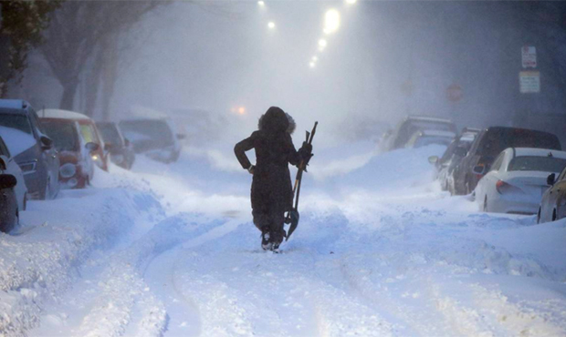 A woman walks down snow-covered Maverick Street in the East Boston neighborhood of Boston, Thursday...