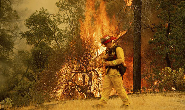 A firefighter walks near flames from the Carr Fire in Redding, Calif., on Saturday, July 28, 2018. ...