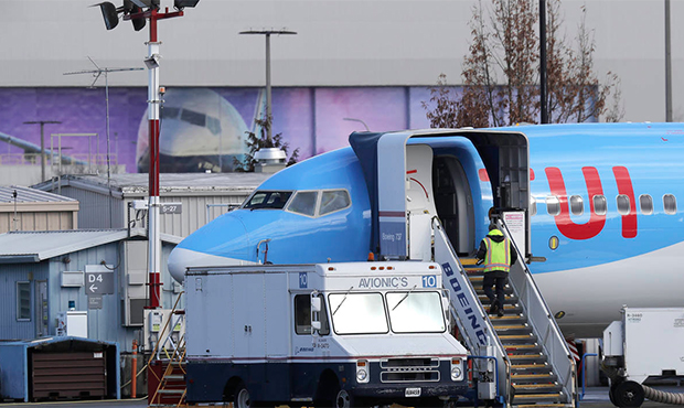 A worker walks up steps to the right of an avionics truck parked next to a Boeing 737 MAX 8 airplan...