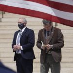 Wyoming Gov. Mark Gordon, right, with an unidentified bodyguard left, reads a prayer to protesters at the state Capitol in Cheyenne on Monday, April 20, 2020. The crowd of about 100 people were protesting school and business shutdowns to limit the spread of the coronavirus. (AP Photo/Mead Gruver)