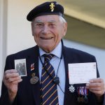 World War II veteran Bill Ridgewell, 94, shows a picture of himself at the age of 16 in uniform and a postcard he got from a French student Marion Nivard and others in Shaftesbury, England, Wednesday, May 6, 2020. As V-E Day approached, Nivard and her classmates in the Normandy region thought of 94-year-old Bill Ridgewell and other vets living in isolation because of the COVID-19 pandemic -- just as they were. The teens decided to swap stories with the men about their lives under lockdown. (AP Photo/Frank Augstein)