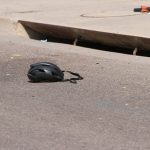 In this Saturday, June 19, 2021, photo courtesy of The White Mountain Independent a cyclist's helmet lies in the road near a damaged bike in Show Low, Ariz. A driver in a pickup truck plowed into bicyclists competing in a community road race in Arizona on Saturday, critically injuring several riders before police chased down the driver and shot him outside a nearby hardware store, police said. (Jim Headley/The White Mountain Independent via AP)