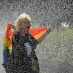 
              A woman with a rainbow flag cools off in a sprinkler ahead of the Equality Parade, the largest LGBT pride parade in Central and Eastern Europe, in Warsaw, Poland, Saturday, June 19, 2021.(AP Photo/Czarek Sokolowski)
            