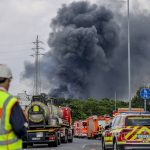 
              Emergency vehicles of the fire brigade, rescue services and police stand not far from an access road to the Chempark over which a dark cloud of smoke is rising in Leverkusen, Germany, Tuesday, July 27, 2021.. After an explosion, fire brigade, rescue services and police are currently in large-scale operation, the police explained. (Oliver Berg/dpa via AP)
            