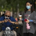 
              Women wearing face masks to help curb the spread of the coronavirus walk past a masked man browsing his smartphone on his bike in Beijing, Tuesday, July 20, 2021. (AP Photo/Andy Wong)
            