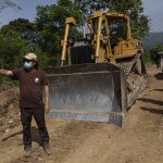 
              Friar Leopoldo Serrano shows bulldozer operators which direction he would like them to pave a road for a new community being constructed for the residents of La Reina, whose homes were devastated by a mudslide triggered by Hurricanes Eta and Iota, in Mission San Francisco de Asis, Honduras, Tuesday, June 22, 2021. Twenty-five years ago, the powerful local cartel run by Arnulfo Valle bought the 70 acres adjacent to the mission where Father Serrano hopes to put those displaced from La Reina. (AP Photo/Rodrigo Abd)
            