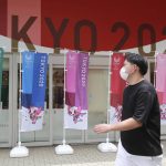 
              A man wearing a face mask to protect against the spread of the coronavirus walks by flags to promote the Olympic Games in Tokyo Monday, July 26, 2021. (AP Photo/Koji Sasahara)
            