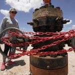 
              Ashley Williams Watt looks at an abandoned well wrapped with locks and chains on her ranch, Friday, July 9, 2021, near Crane, Texas. Some of her wells are leaking chemicals such as benzene, a known carcinogen, into fields and drinking water. (AP Photo/Eric Gay)
            