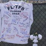 
              Members of the Florida Task Force 8 leave an autograph shirt signed by team members pinned to the memorial site fence on Sunday, July 4, 2021, in Surfside, Fla. Demolition specialists carefully bored holes to insert explosive charges into the precarious, still-standing portion of a collapsed South Florida condo building that will come down to open up new areas for rescue teams to search. A top Miami-Dade fire official said 80% of the drilling work was complete and the remaining structure could come down as soon as Sunday night. (Carl Juste/Miami Herald via AP)
            
