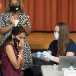 
              Ariel Quero, 16, left, a student at Lehman High School, reacts after getting the Pfizer COVID-19 vaccine from Katrina Taormina, right, Tuesday, July 27, 2021, in New York. Schools Chancellor Meisha Porter applauds behind her. The Centers for Disease Control and Prevention is urging everyone in K-12 schools to wear a mask when they return to class, regardless of vaccination status. (AP Photo/Mark Lennihan)
            