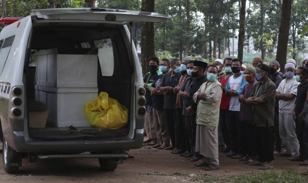 Residents pray outside an ambulance carrying coffins of two COVID-19 victims before their burial at...