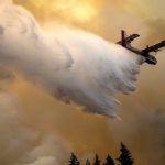 
              A scoop plane drops water onto a burning ridge where a fire line had been created by crews of wildland firefighters, Monday, July 12, 2021, at the Lick Creek Fire, south of Asotin, Wash. (Pete Caster/Lewiston Tribune via AP)
            