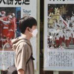 
              A man wearing face masks to protect against the spread of the coronavirus walks past extra papers reporting the start of the Tokyo Olympics in Tokyo Saturday, July 24, 2021. (AP Photo/Koji Sasahara)
            