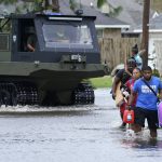 
              Michael Thomas, back, carries his daughter Mikala, out of his flooded neighborhood while a high water rescue vehicle moves past after Hurricane Ida moved through Monday, Aug. 30, 2021, in LaPlace, La. (AP Photo/Steve Helber)
            