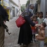 
              A police officer stand guard while a health worker administers a polio vaccine to a child in Peshawar, Pakistan, Friday, July 30, 2021. The Pakistani government launched an anti-polio vaccination campaign in an effort to eradicate the crippling disease. (AP Photo/Muhammad Sajjad)
            