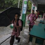 Students arrive amid heavy rains on the first day of partial reopening of schools in Noida, a suburb of New Delhi, India, Wednesday, Sept. 1, 2021. Many students in India will be able to step inside a classroom for the first time in nearly 18 months from Wednesday, as authorities have given the green light to partially reopen schools despite apprehension from some parents and signs that coronavirus infections are picking up again. Schools and colleges in least six states will reopen in a gradual manner with health measures in place throughout September. In New Delhi, all staff must be vaccinated and class sizes will be capped at 50% with staggered seating and sanitized desks. (AP Photo/Altaf Qadri)