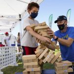 
              While wearing masks, David Bingener, 11, center, and Mark Bingener, right, play Jenga while tailgating before an NCAA college football game between the Hawaii Warriors and the UCLA Bruins, Saturday, Aug. 28, 2021, in Pasadena, Calif. California is seeing lower coronavirus transmission than other U.S. states as virus cases and hospitalizations decline following a summer surge. State health experts say relatively high vaccination rates ahead of the arrival of the delta variant made a difference. (AP Photo/Ashley Landis)
            