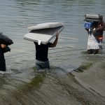 Haitian migrants carry provisions as they use a dam to cross into the United States from Mexico, Saturday, Sept. 18, 2021, in Del Rio, Texas. U.S. officials said that within the next three days, they plan to ramp up expulsion flights for some of the thousands of Haitian migrants who have gathered in the Texas city from across the border in Mexico. (AP Photo/Eric Gay)