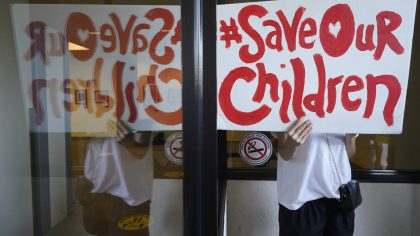 An anti-vaccine mandate protester holds a sign outside the front windows of the Los Angeles Unified...