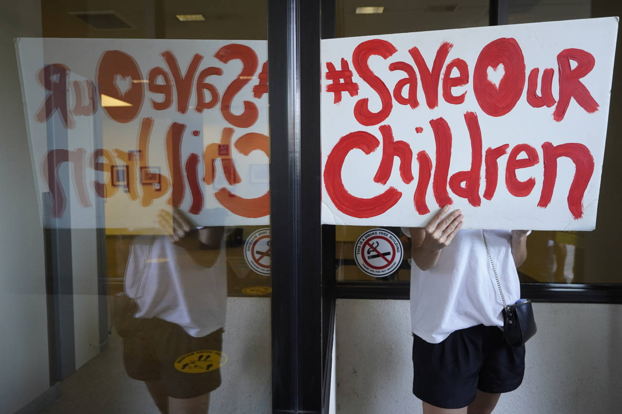 An anti-vaccine mandate protester holds a sign outside the front windows of the Los Angeles Unified...