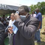
              Funeral director Shawn Troy wipes away perspiration during a graveside service at Hillcrest Cemetery outside Mullins, S.C., on Monday, May 24, 2021. His father, William Penn Troy Sr., died of COVID-19 in August 2020, one of many Black morticians to succumb during the pandemic. (AP Photo/Allen G. Breed)
            