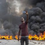 
              A protester takes a selfie at a burning barricade set by protesters in Port-au-Prince, Haiti, Monday, Oct. 18, 2021. Workers angry about the nation’s lack of security went on strike in protest two days after 17 members of a U.S.-based missionary group were abducted by a violent gang. (AP Photo/Joseph Odelyn)
            