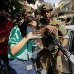 
              A Lebanese teacher who who is afraid of the sounds from nearby armed clashes, flees a school under the protection of Lebanese soldiers after a clashes erupted along a former 1975-90 civil war front-line between Muslim Shiite and Christian areas at Ain el-Remaneh neighborhood, in Beirut, Lebanon, Thursday, Oct. 14, 2021. Armed clashes broke out in Beirut Thursday during the protest against the lead judge investigating last year's massive blast in the city's port, as tensions over the domestic probe boiled over. (AP Photo/Hussein Malla)
            