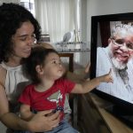 
              Luna Tarsila points to her grandfather Juracy Cruz Junior, who died of COVID-19, as she sits on the lap her mother, Fernanda Natasha Bravo Cruz, in their home in Brasilia, Brazil, Thursday, Oct. 21, 2021. A Brazilian Senate committee investigating the government’s pandemic response, culminated on Oct. 26, 2021, with the recommendation President Jair Bolsonaro be indicted for crimes, along with dozens of other officials and allies. (AP Photo/Eraldo Peres)
            