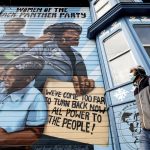 
              A man passes a mural celebrating the Black Panther Party in Oakland, Calif., on Wednesday, Oct. 13, 2021. The home sits across the street from where Black Panther Party co-founder Huey Newton was shot and killed in 1989. A lesser-known fact was that a majority of the party's membership, as well as its leadership outside of the central organizing committee in Oakland, were Black women. (AP Photo/Noah Berger)
            