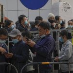 Service sector workers wearing face masks to help curb the spread of the coronavirus check on their scanned code as they lining up to receive a swab for the COVID-19 test during a mass testing in Beijing, Friday, Oct. 29, 2021, following a spike of the coronavirus in the capital and other provincials. (AP Photo/Andy Wong)