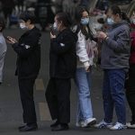 
              A woman wearing a face mask to help curb the spread of the coronavirus walks through a line of masked service sector women waiting to receive a swab for the COVID-19 test during a mass testing in Beijing, Friday, Oct. 29, 2021, following a spike of the coronavirus in the capital and other provincials. (AP Photo/Andy Wong)
            