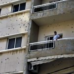 
              A man stands on his balcony riddled by bullets from deadly clashes that erupted Thursday along a former 1975-90 civil war front-line between Muslim Shiite and Christian areas, in Ain el-Remaneh neighborhood, Beirut, Lebanon, Friday, Oct. 15, 2021. Schools, banks and government offices across Lebanon shut down Friday after hours of gun battles between heavily armed militias killed six people and terrorized the residents of Beirut. (AP Photo/Bilal Hussein)
            