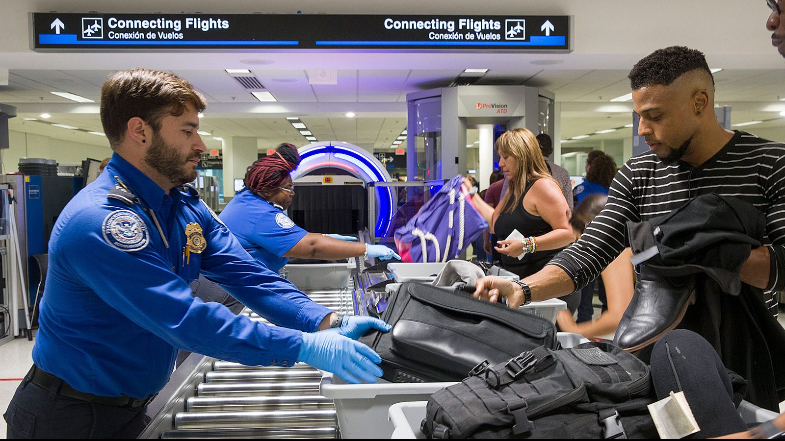 Transportation Security Administration (TSA) agents help travelers place their bags through the 3-D...