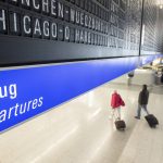 A flight to Chicago O'Hare in the USA is displayed on a board at Frankfurt airport under which passengers with suitcases walk along in Frankfurt, Germany, Monday, Nov. 8, 2021. From 8 November, flights with vaccinated EU citizens to the USA will be allowed again. (Sebastian Gollnow/dpa via AP)