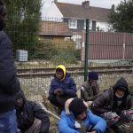 
              FILE- Migrants wait for food distribution at a camp in Calais, northern France, Thursday, Oct. 14, 2021. The price to cross the English Channel varies according to the network of smugglers, between 3,000 and 7,000 euros. Often, the fee also includes a very short-term tent rental in the windy dunes of northern France and food cooked over fires that sputter in the rain that falls for more than half the month of November in the Calais region. (AP Photo/Christophe Ena, File)
            